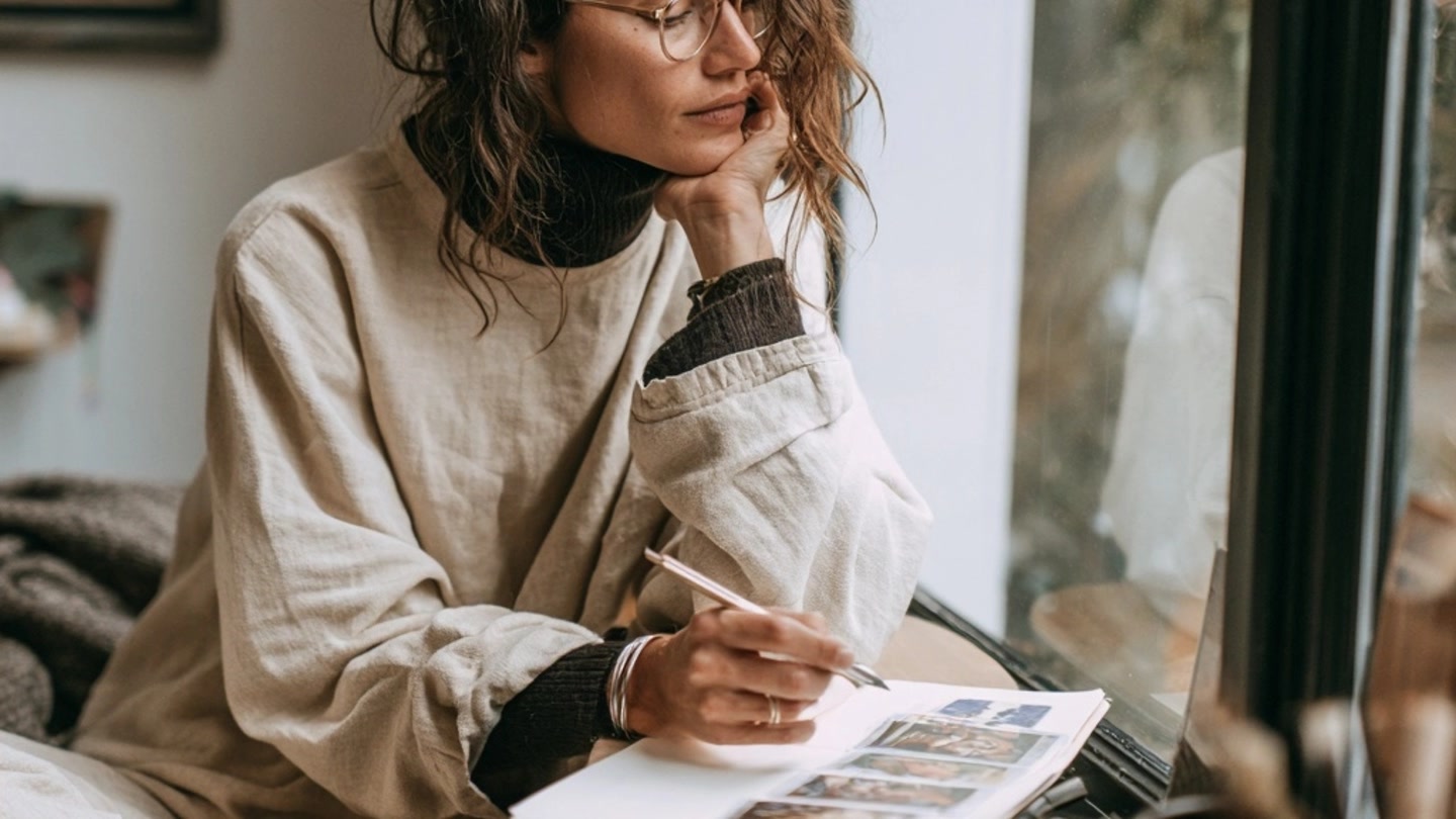 Personne comparant des cartes de tarot à ses notes près d’une fenêtre
