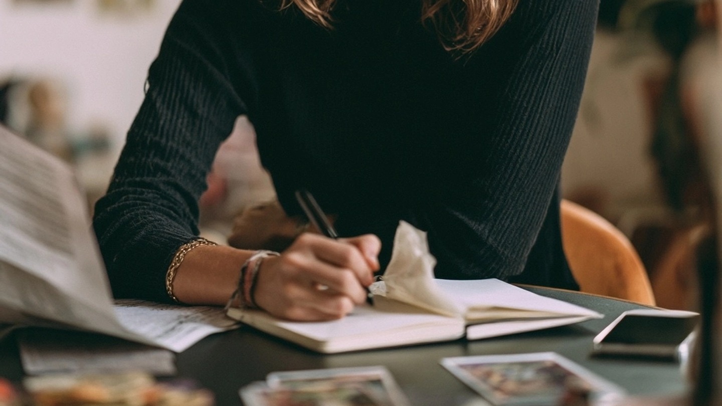 Mains écrivant dans un carnet avec des cartes posées sur la table